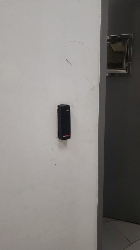 Wall-mounted electronic card reader installed beside a secured doorway for controlled access entry.