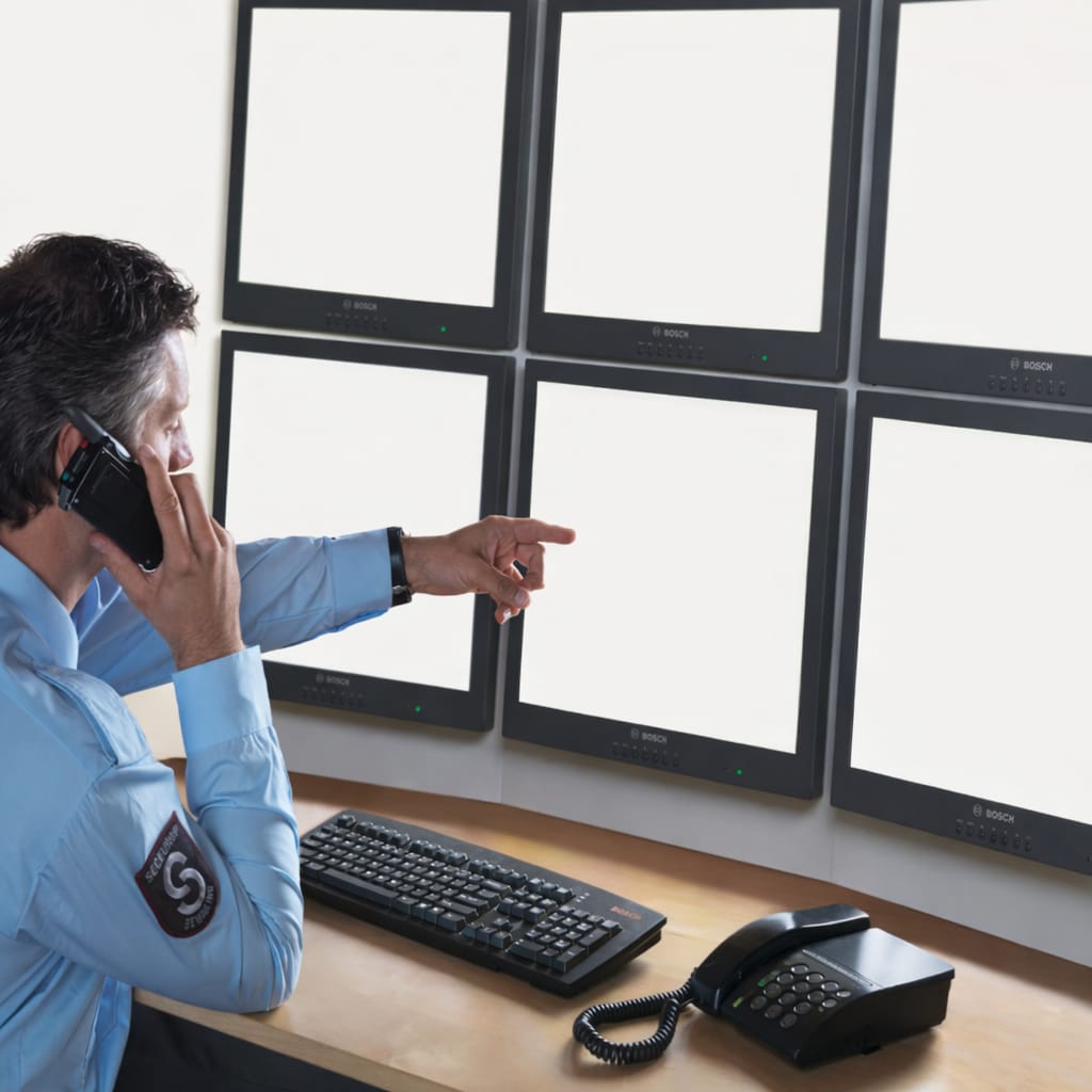 Security operator monitoring multiple CCTV surveillance screens in a control room for industrial facility protection.
